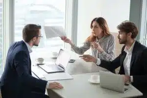 trois professionnels en réunion discutent autour d'une table avec ordinateurs portables