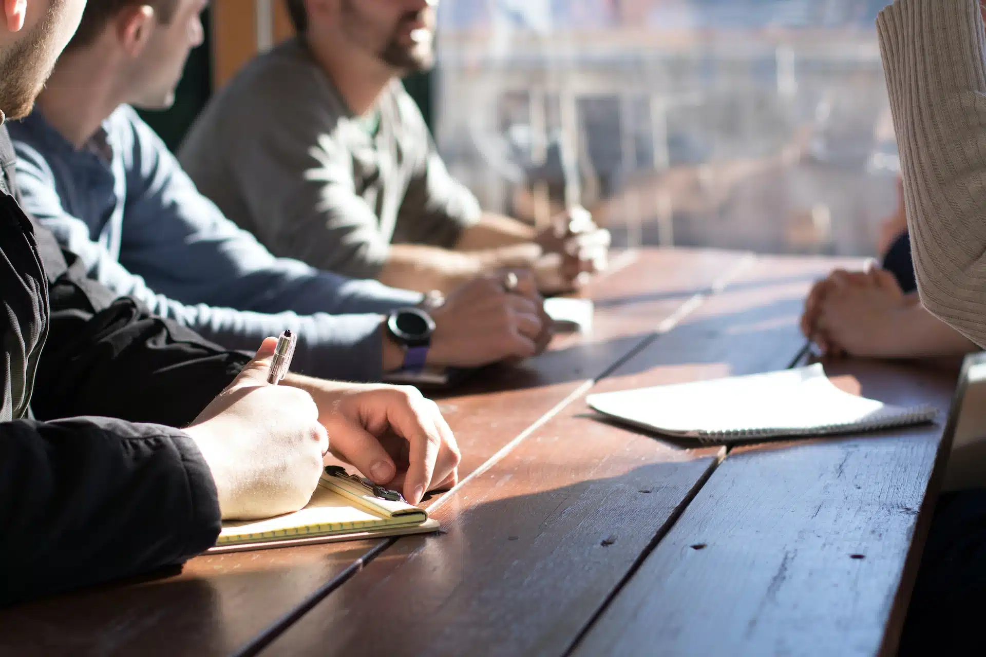 Un groupe de personnes d'une entreprise assises autour d'une table en bois, discutant d'attestation de domiciliation.