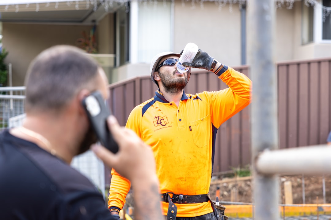 A construction worker drinks water while another talks